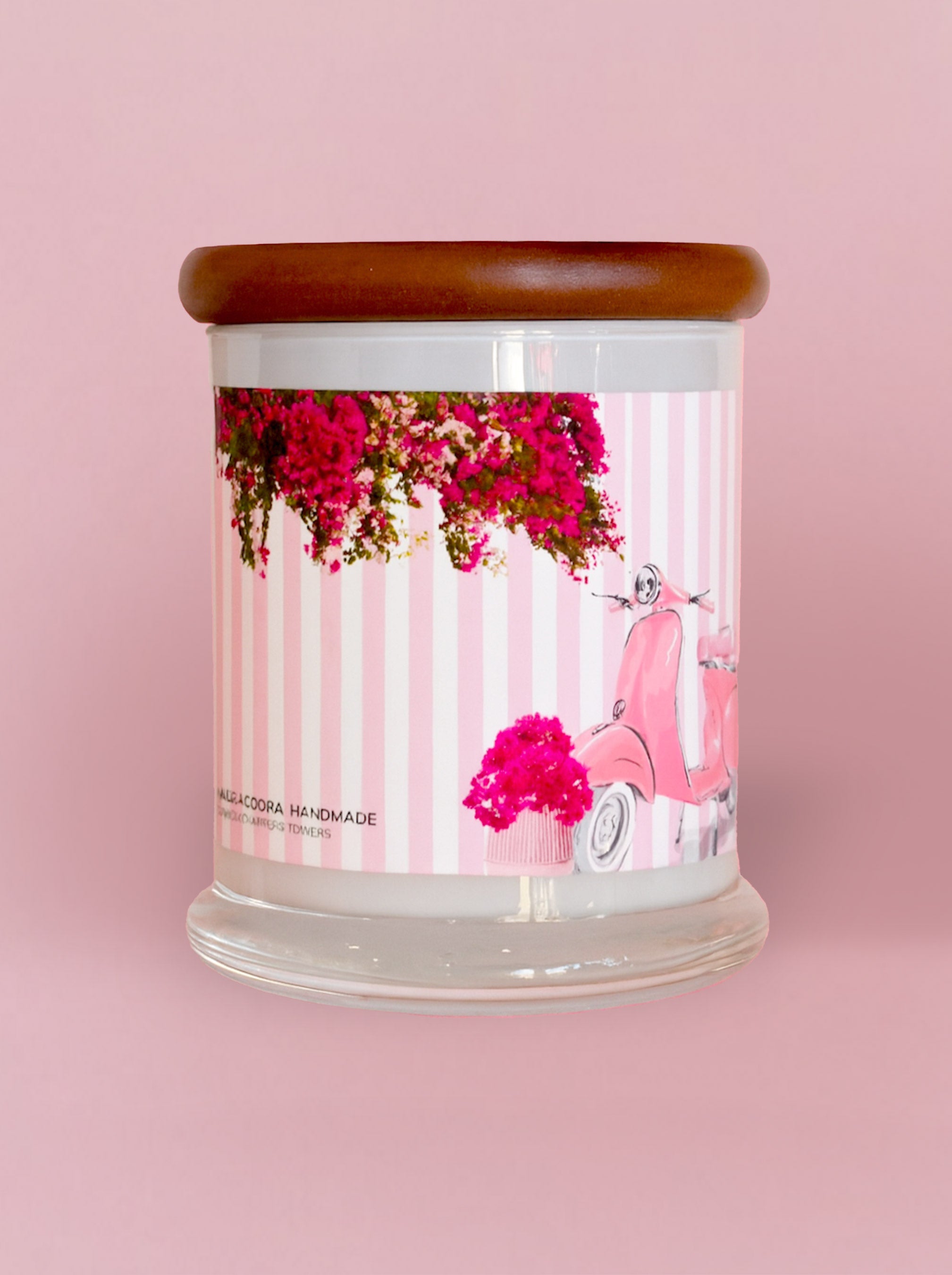 Candle with a decorative label featuring a pink scooter and flowers on a pink background