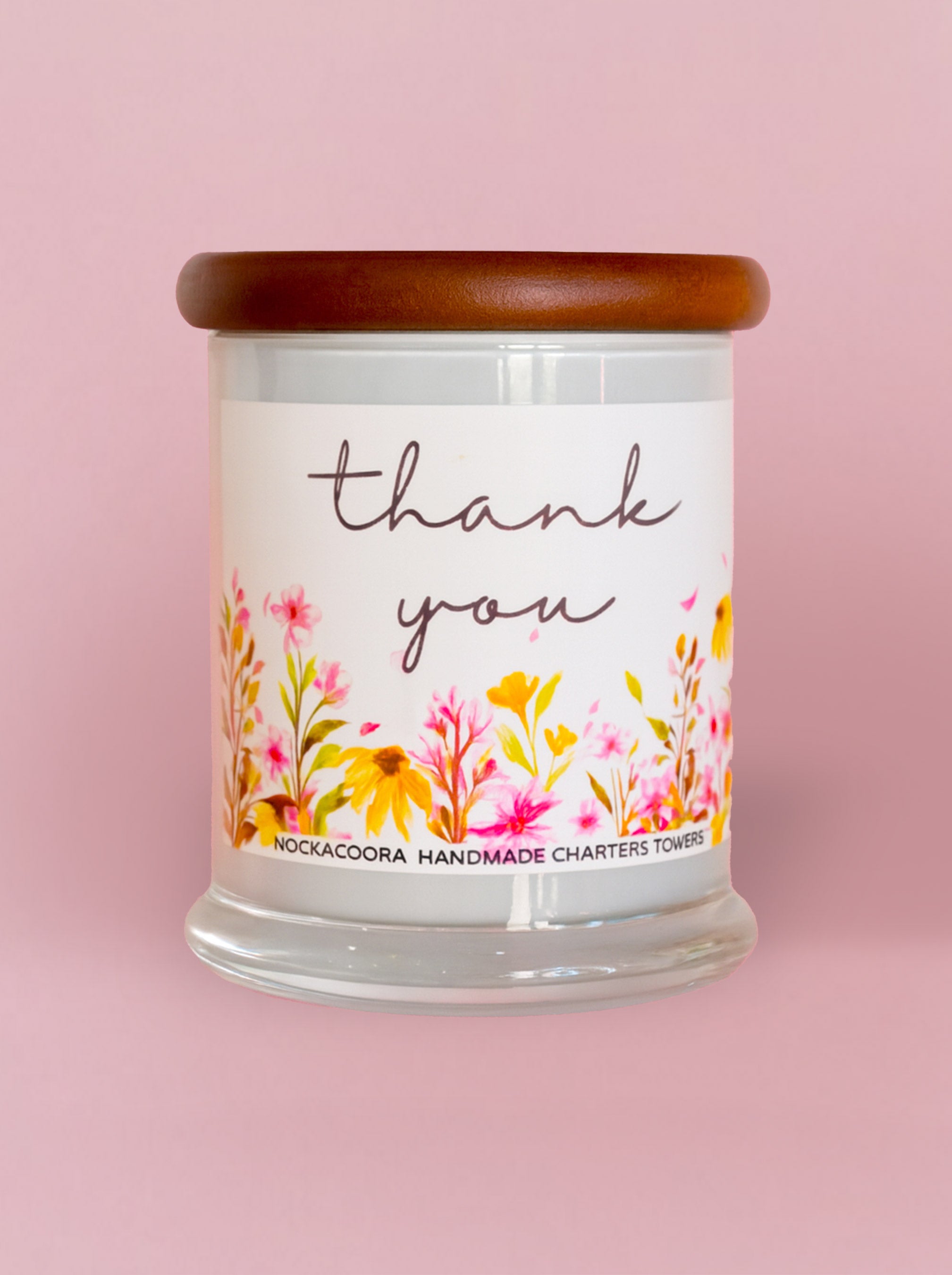 Candle with 'thank you' label and floral design on a pink background